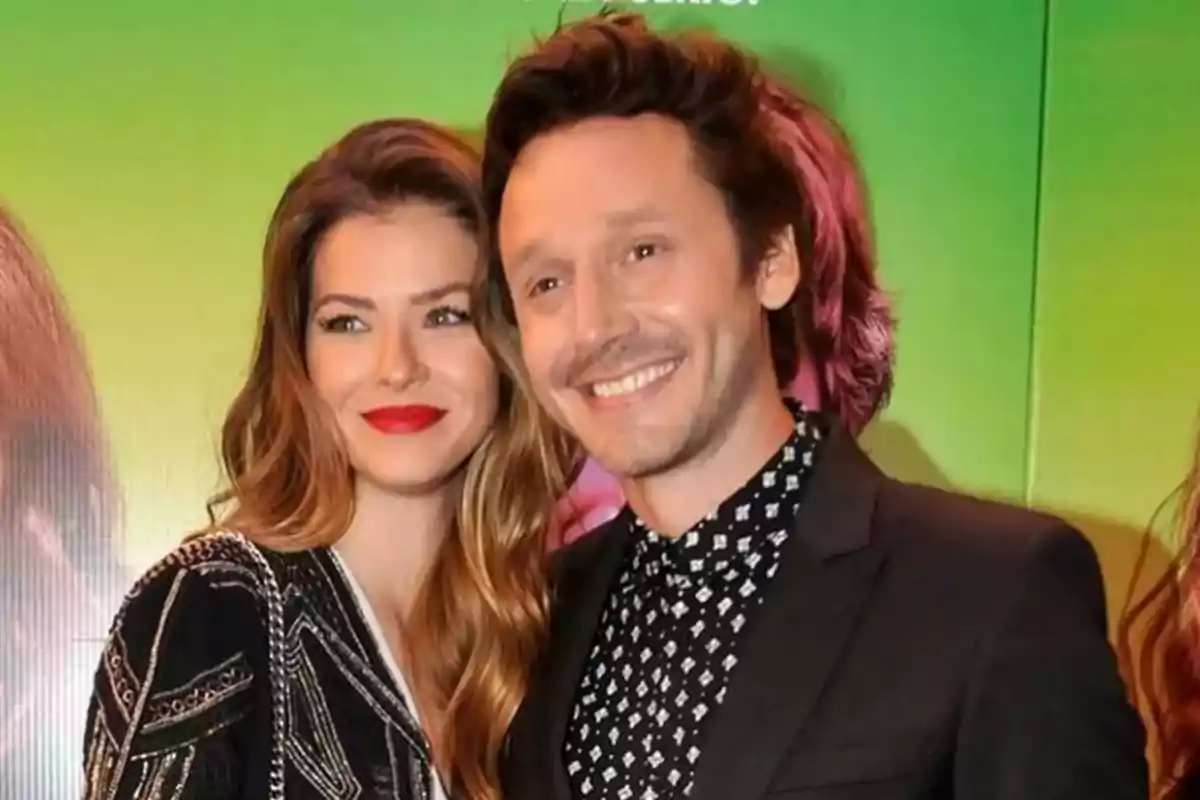 Couple smiling in front of a green background at an event