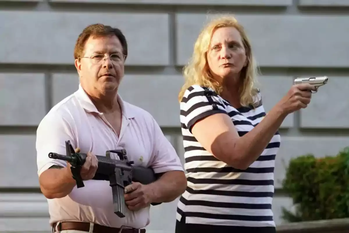 Una pareja de personas adultas sostiene armas de fuego en un entorno urbano al aire libre, ambos miran hacia el frente con expresiones serias.