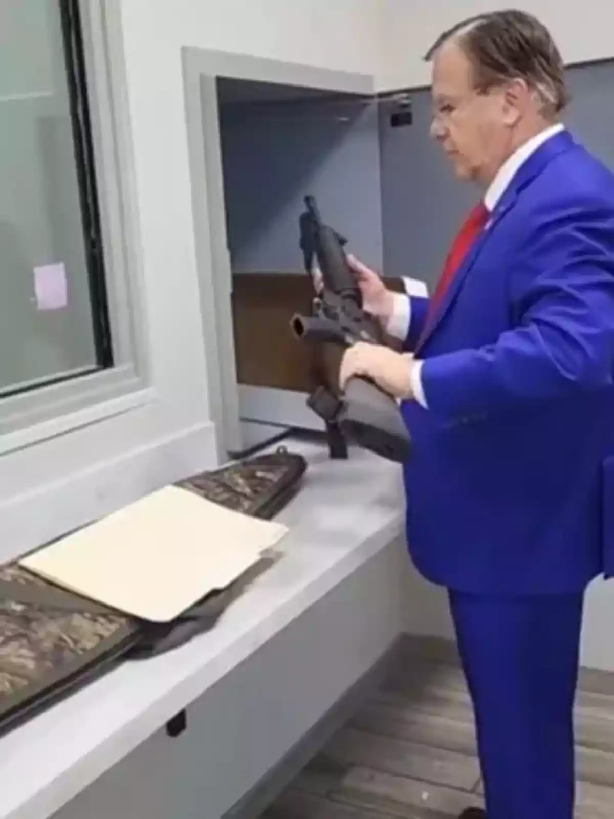 Hombre de traje azul y corbata roja manipulando un arma larga en una mesa dentro de una habitación cerrada Hombre de traje azul y corbata roja manipulando un arma larga en una mesa dentro de una habitación cerrada