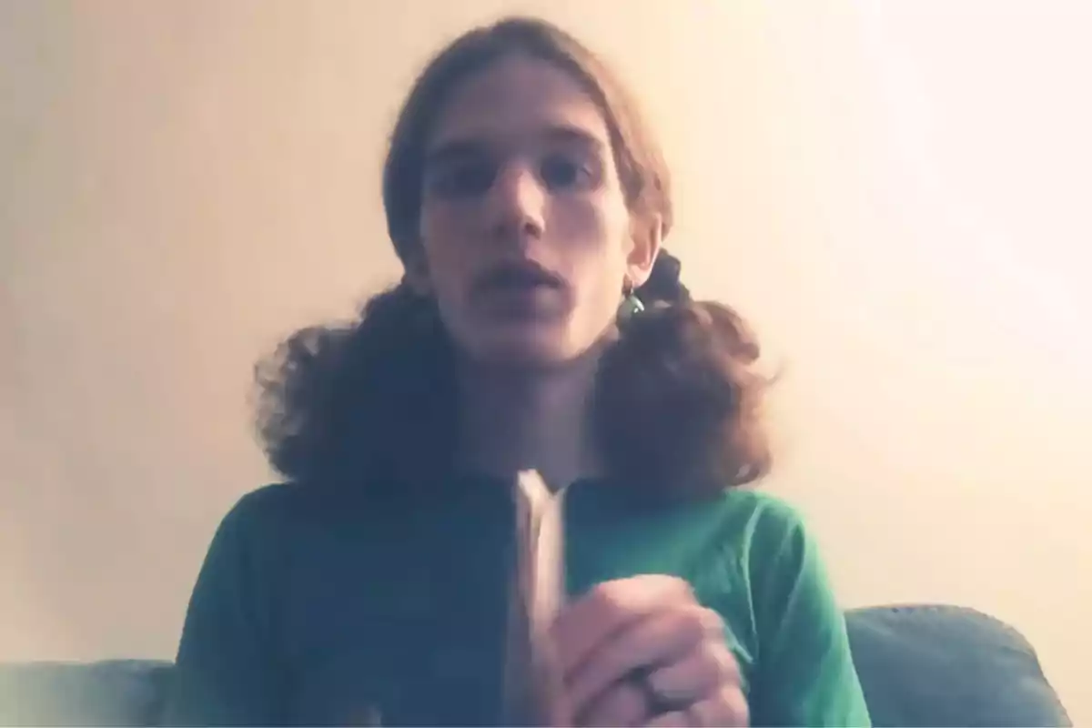 Person with long, curly hair in pigtails, wearing a green t-jersey and holding an object in front of a light-colored wall. Person with long, curly hair in pigtails, wearing a green t-jersey and holding an object in front of a light-colored wall.