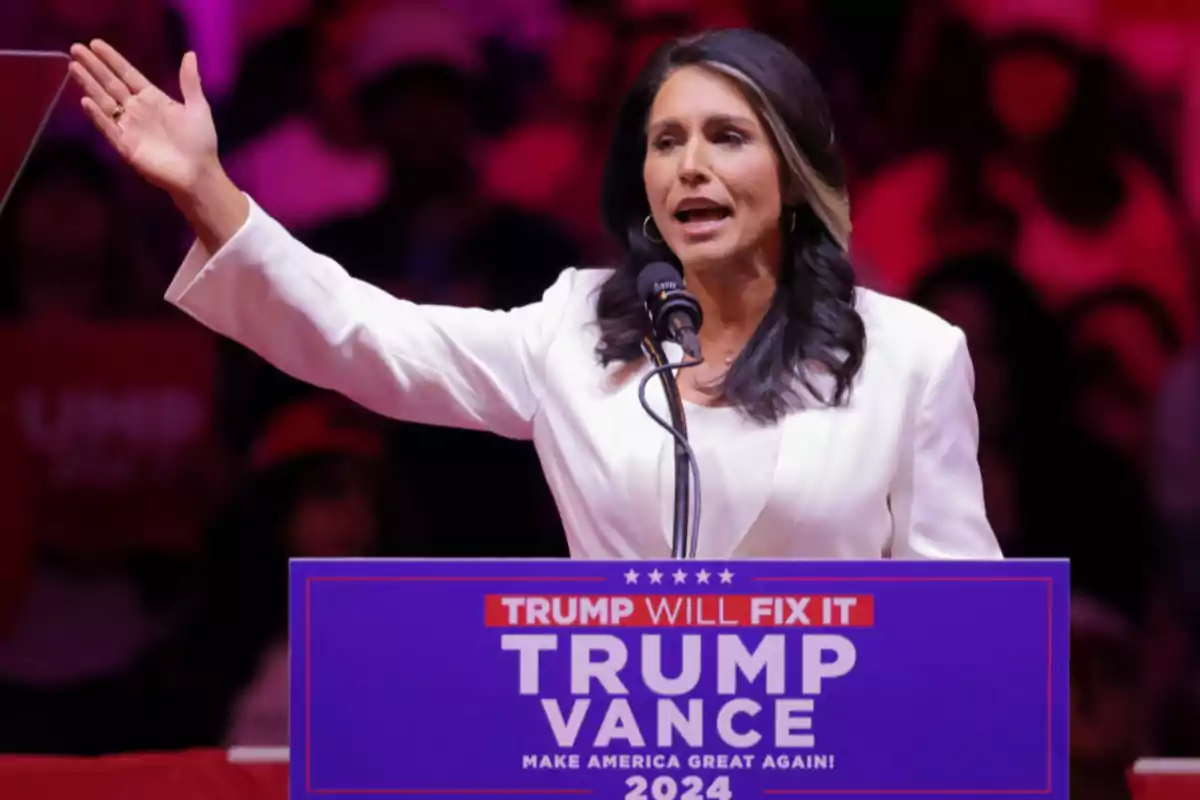 Dark-haired woman in a white blazer speaking at a political rally behind a podium with the sign Trump Vance 2024 Make America Great Again