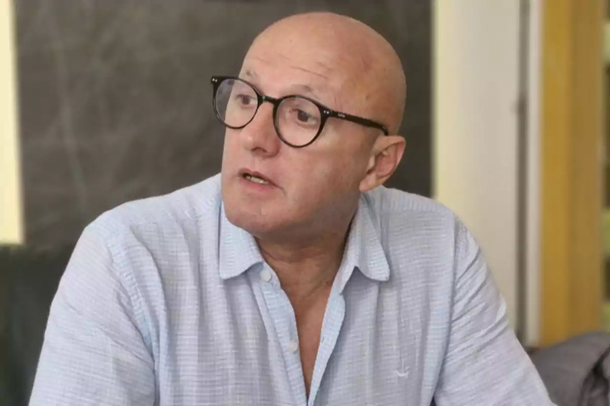 Hombre calvo con gafas y camisa clara sentado en un interior mirando hacia un lado Hombre calvo con gafas y camisa clara sentado en un interior mirando hacia un lado