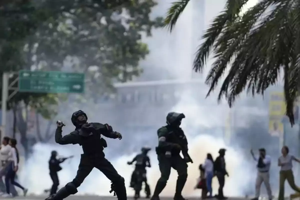 Policías antidisturbios lanzan gases lacrimógenos durante una protesta en una calle rodeada de humo y personas corriendo