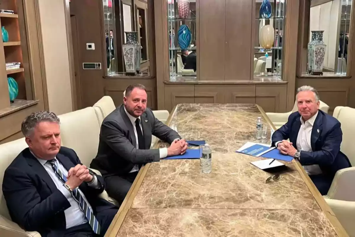 Tres hombres con traje sentados alrededor de una mesa de mármol en una sala de reuniones elegante Tres hombres con traje sentados alrededor de una mesa de mármol en una sala de reuniones elegante