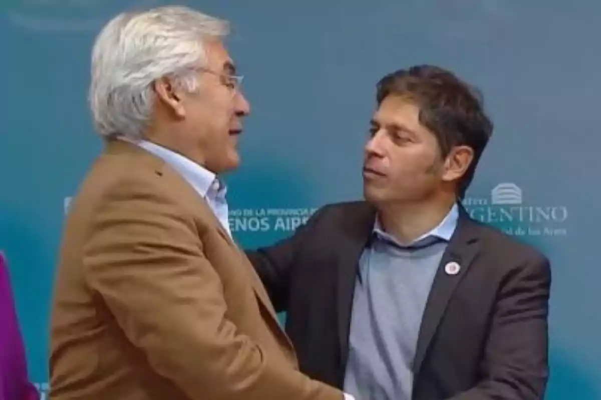 Dos hombres de traje se saludan y conversan en un evento formal frente a un fondo azul Dos hombres de traje se saludan y conversan en un evento formal frente a un fondo azul
