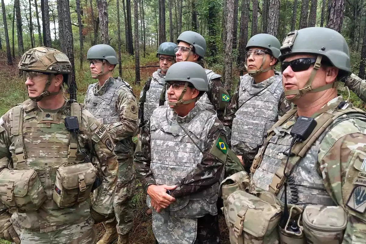 Grupo de soldados con uniformes de camuflaje y cascos en un bosque, algunos llevan parches con la bandera de Brasil y otros con insignias militares estadounidenses, todos observan atentamente hacia un mismo punto. Grupo de soldados con uniformes de camuflaje y cascos en un bosque, algunos llevan parches con la bandera de Brasil y otros con insignias militares estadounidenses, todos observan atentamente hacia un mismo punto.