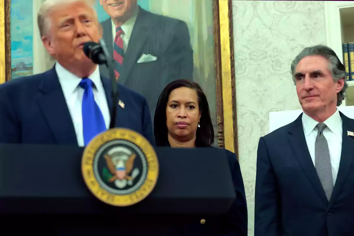 Three people at an official event in a room with a portrait in the background and a presidential podium at the front.