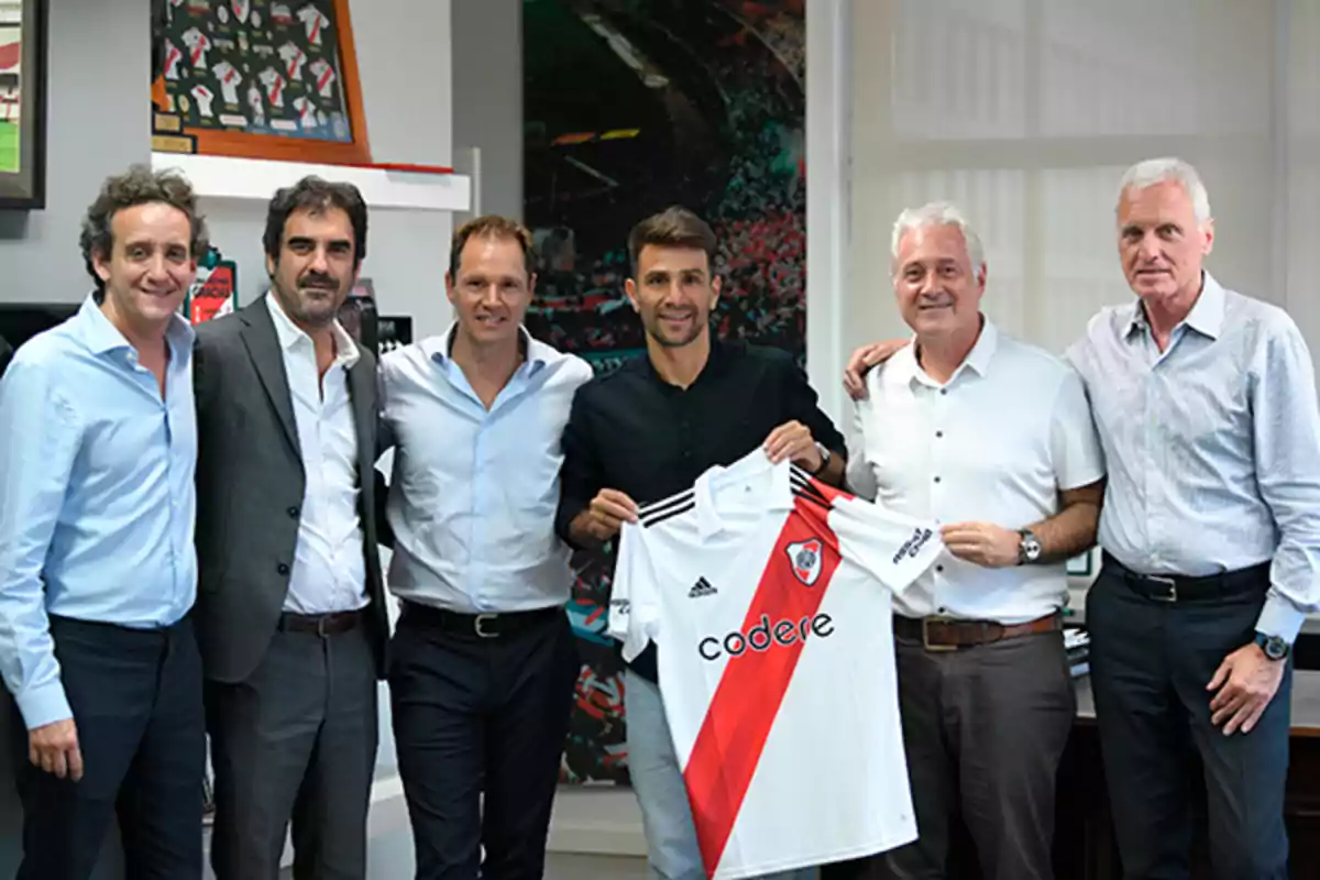 Grupo de seis hombres posando juntos en una oficina mientras uno de ellos sostiene una camiseta de River Plate Grupo de seis hombres posando juntos en una oficina mientras uno de ellos sostiene una camiseta de River Plate