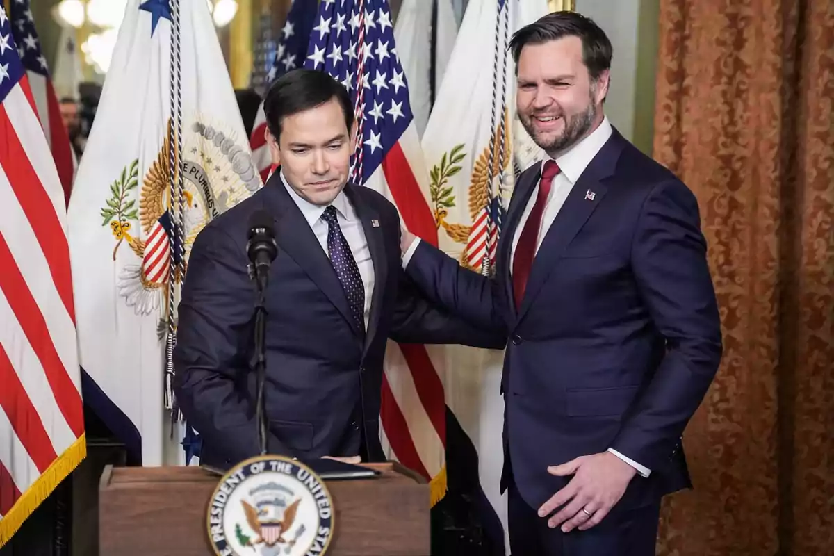 Two men in dark suits are standing in front of several American flags and a podium with the presidential seal; one of them is smiling as he places his hand on the other's shoulder. Two men in dark suits are standing in front of several American flags and a podium with the presidential seal; one of them is smiling as he places his hand on the other's shoulder.