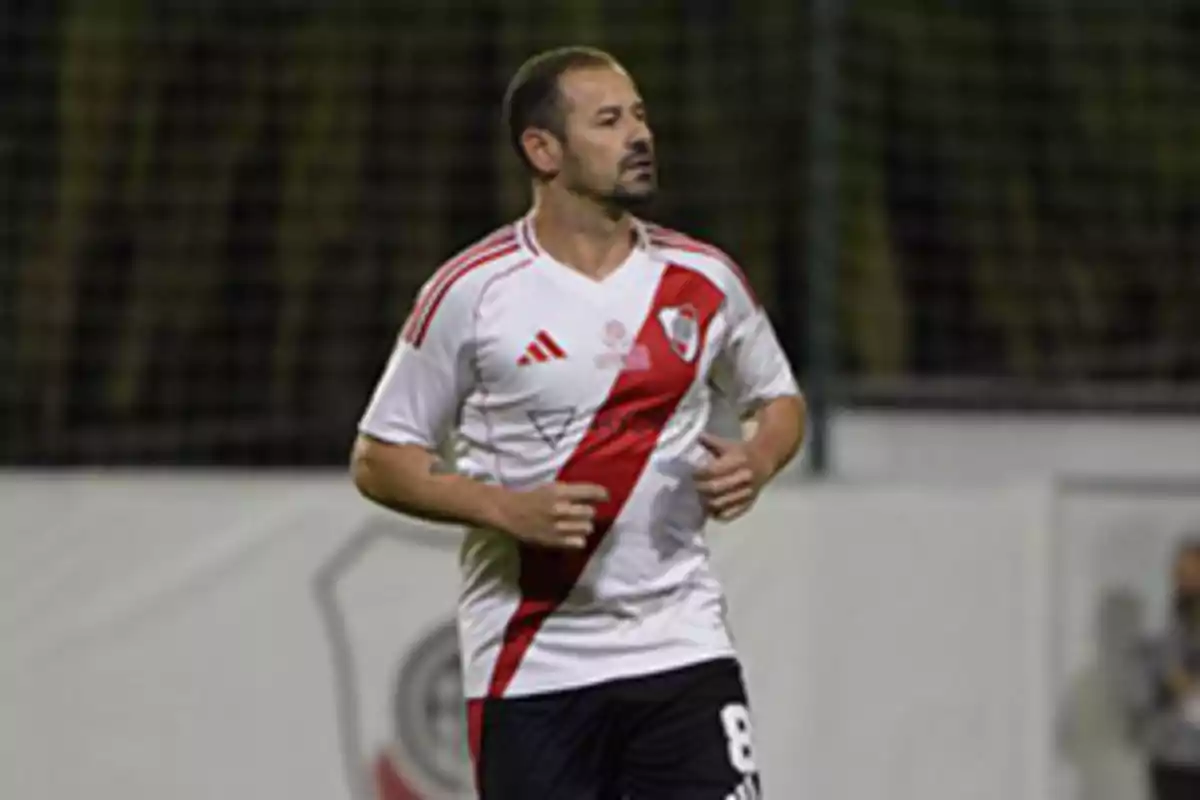 Futbolista con camiseta blanca y banda roja de River Plate corriendo en una cancha Futbolista con camiseta blanca y banda roja de River Plate corriendo en una cancha