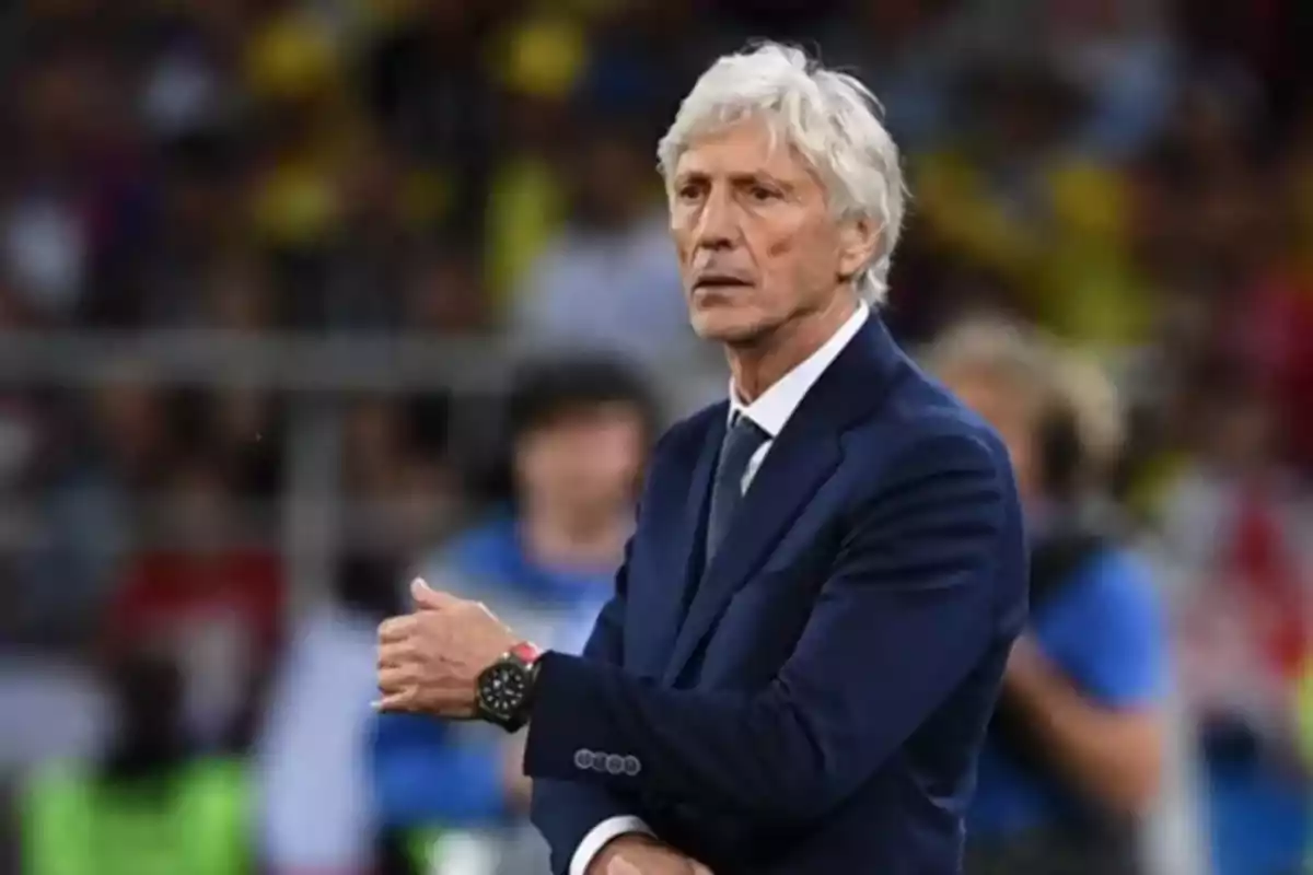 Hombre de cabello canoso con traje azul oscuro y corbata en un estadio de fútbol