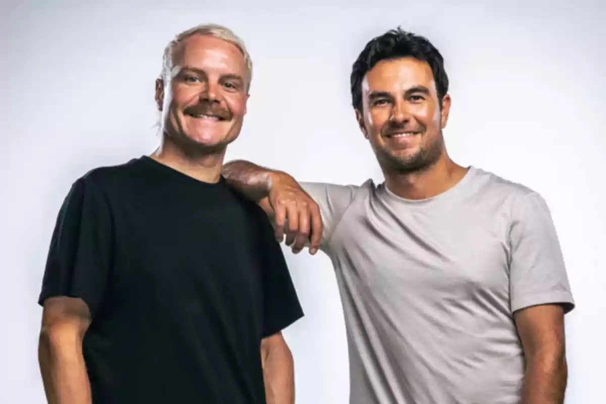 Dos hombres sonrientes posan juntos frente a un fondo claro uno lleva camiseta negra y el otro camiseta gris clara