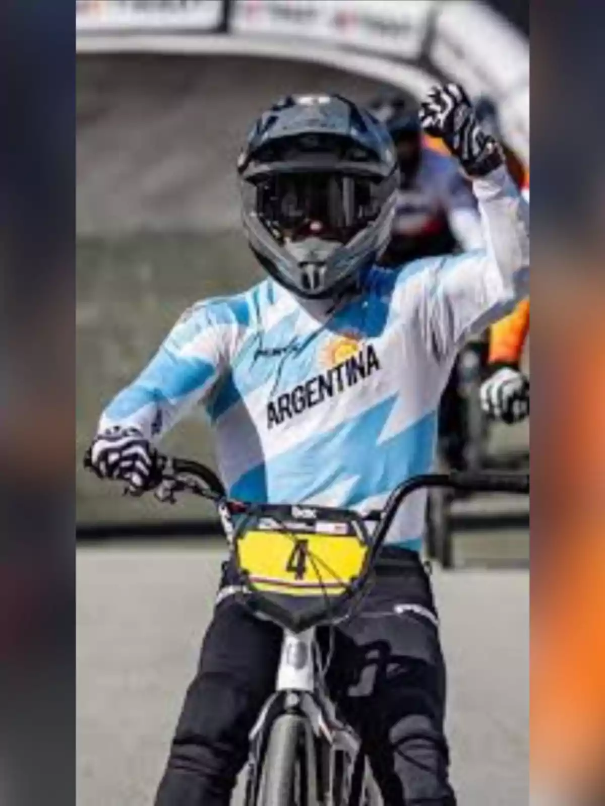 Cyclist wearing a helmet and Argentina uniform raising their arm while competing in a BMX race Cyclist wearing a helmet and Argentina uniform raising their arm while competing in a BMX race