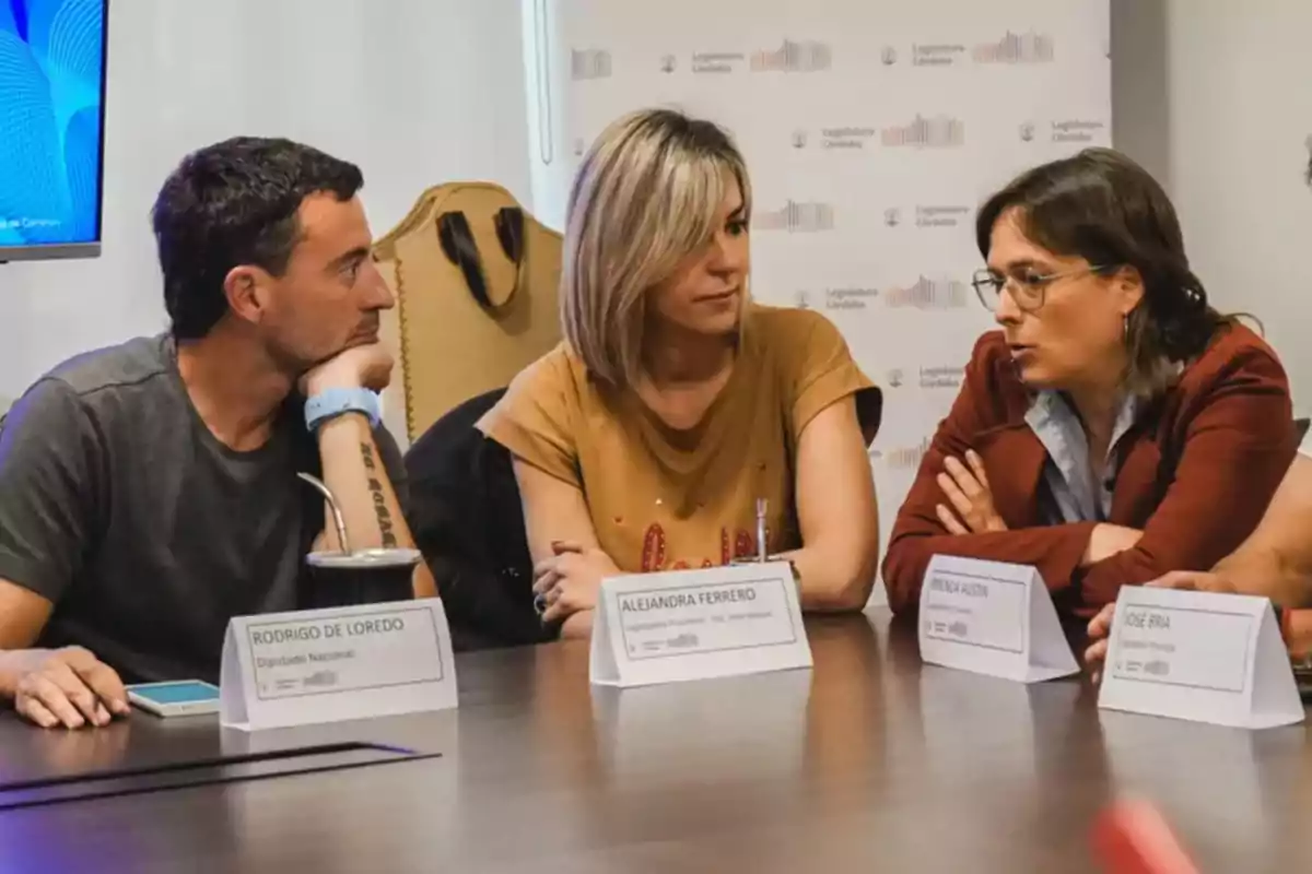 Three people sitting at a meeting table talking, with nameplates in front of them and an institutional backdrop of the Córdoba Legislature. Three people sitting at a meeting table talking, with nameplates in front of them and an institutional backdrop of the Córdoba Legislature.