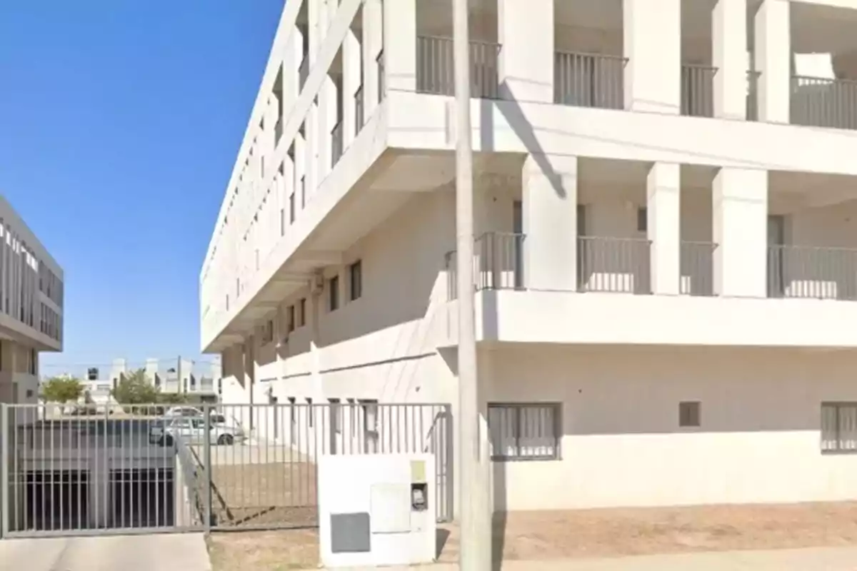 Edificio moderno de varios pisos con balcones y barandales metálicos, portón de acceso y cielo despejado Edificio moderno de varios pisos con balcones y barandales metálicos, portón de acceso y cielo despejado