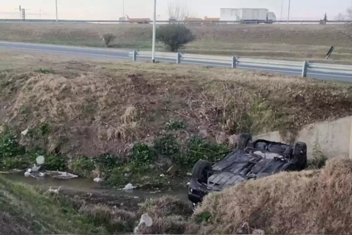 Auto volcado en una zanja junto a una carretera con pasto seco y basura alrededor Auto volcado en una zanja junto a una carretera con pasto seco y basura alrededor