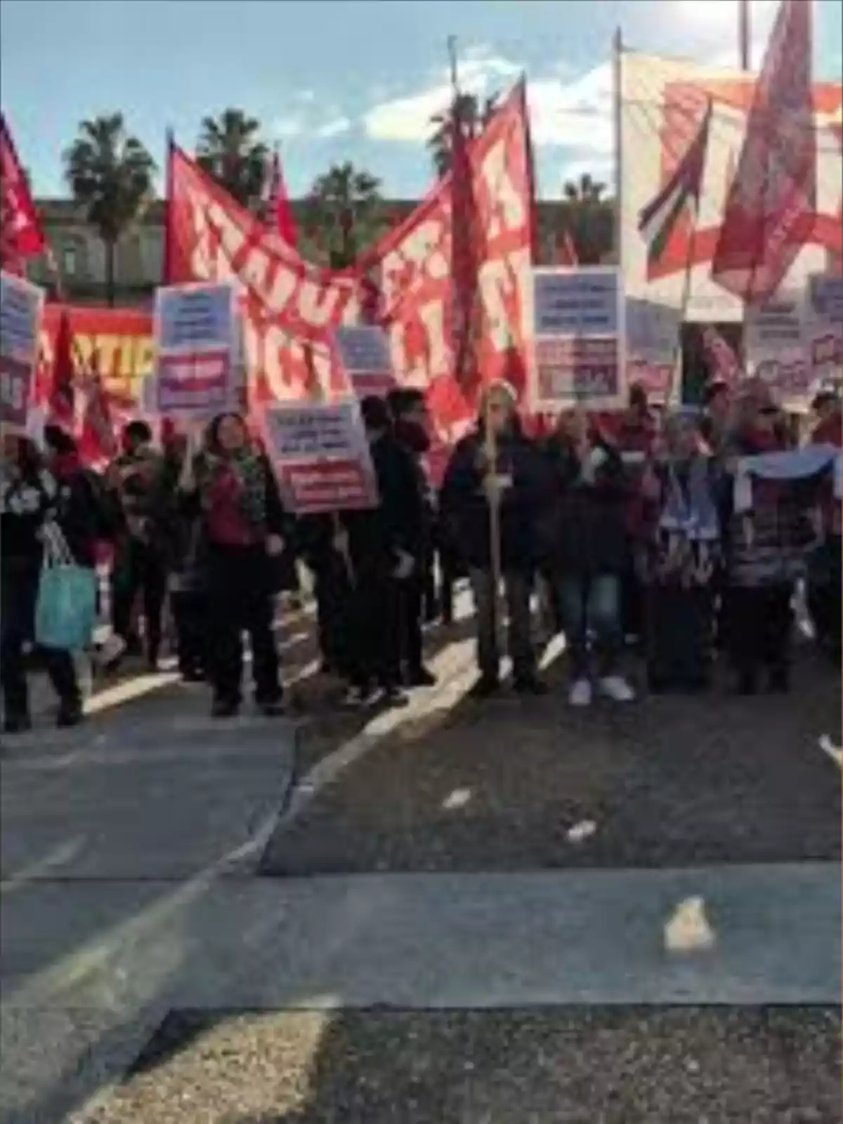 Grupo de personas manifestándose en la calle con pancartas y banderas rojas bajo el sol Grupo de personas manifestándose en la calle con pancartas y banderas rojas bajo el sol