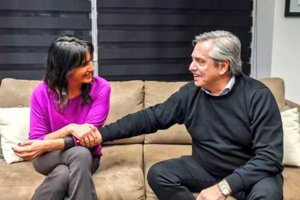 Dos personas sentadas en un sillón se dan la mano y se sonríen mutuamente