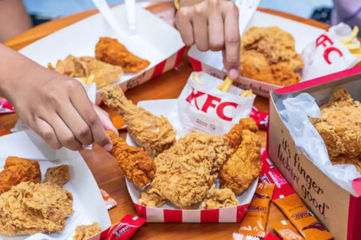 Personas compartiendo piezas de pollo frito y papas fritas de KFC en una mesa