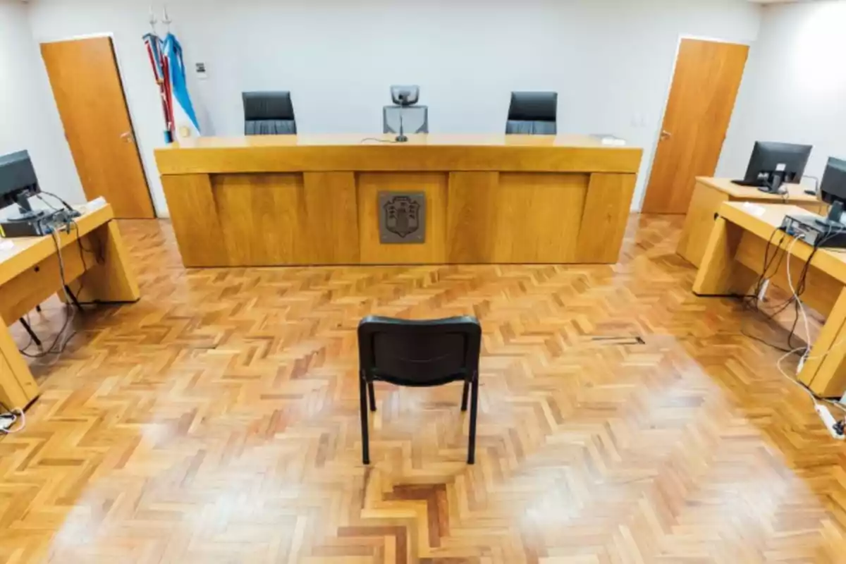 Empty courtroom with a black chair in the center facing a wooden bench and desks with computers on the sides Empty courtroom with a black chair in the center facing a wooden bench and desks with computers on the sides
