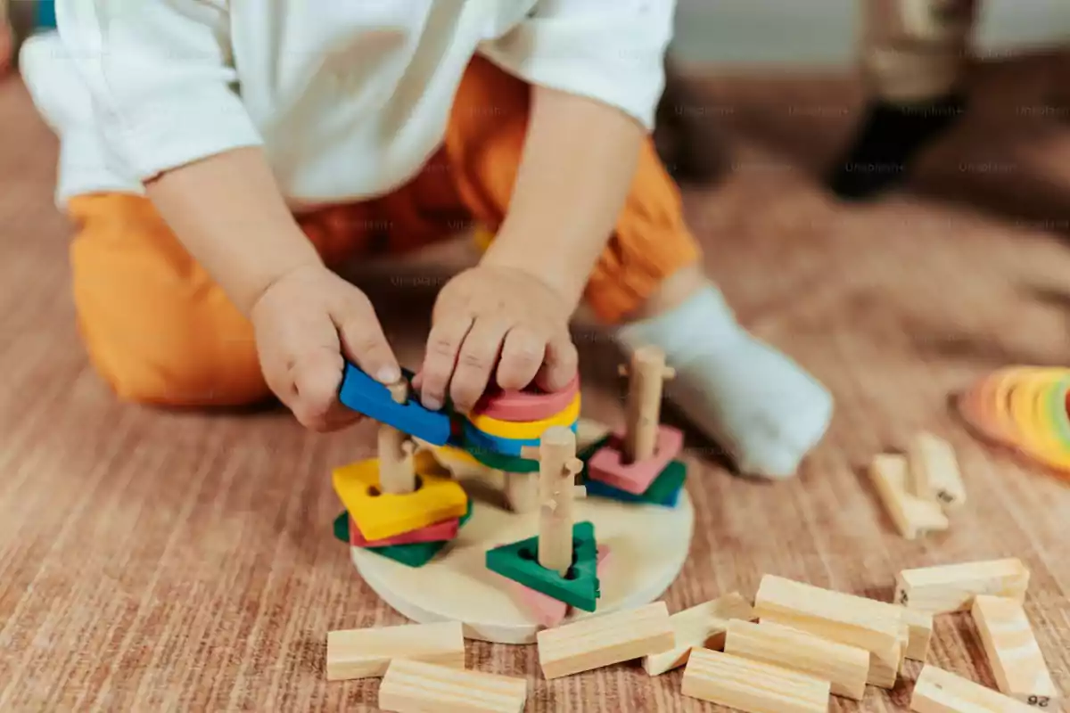 Niño jugando con bloques de madera de colores y piezas geométricas sobre una alfombra Niño jugando con bloques de madera de colores y piezas geométricas sobre una alfombra
