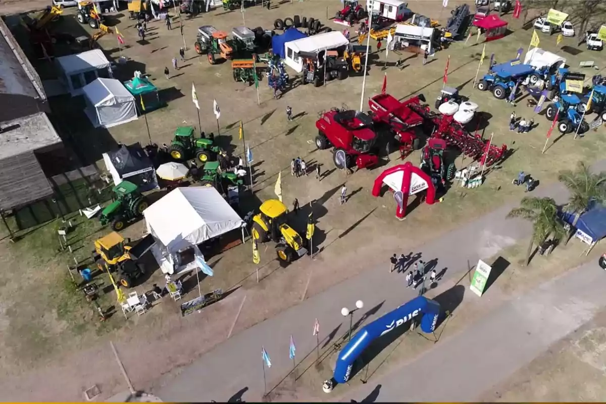 Vista aérea de una exposición agrícola con tractores, maquinaria pesada, carpas y personas recorriendo el predio Vista aérea de una exposición agrícola con tractores, maquinaria pesada, carpas y personas recorriendo el predio