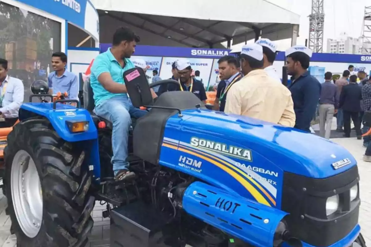 A group of people watches and talks around a blue tractor at an outdoor exhibition. A group of people watches and talks around a blue tractor at an outdoor exhibition.