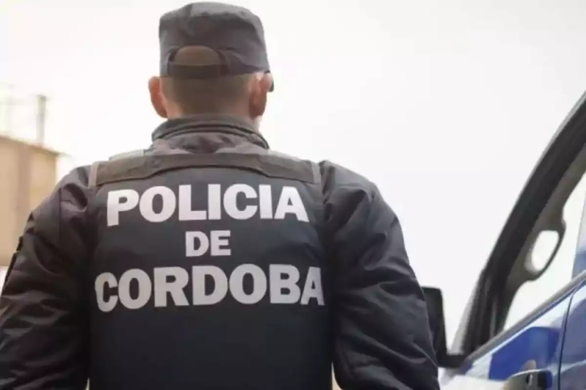 Policía de Córdoba de espaldas junto a una patrulla Policía de Córdoba de espaldas junto a una patrulla