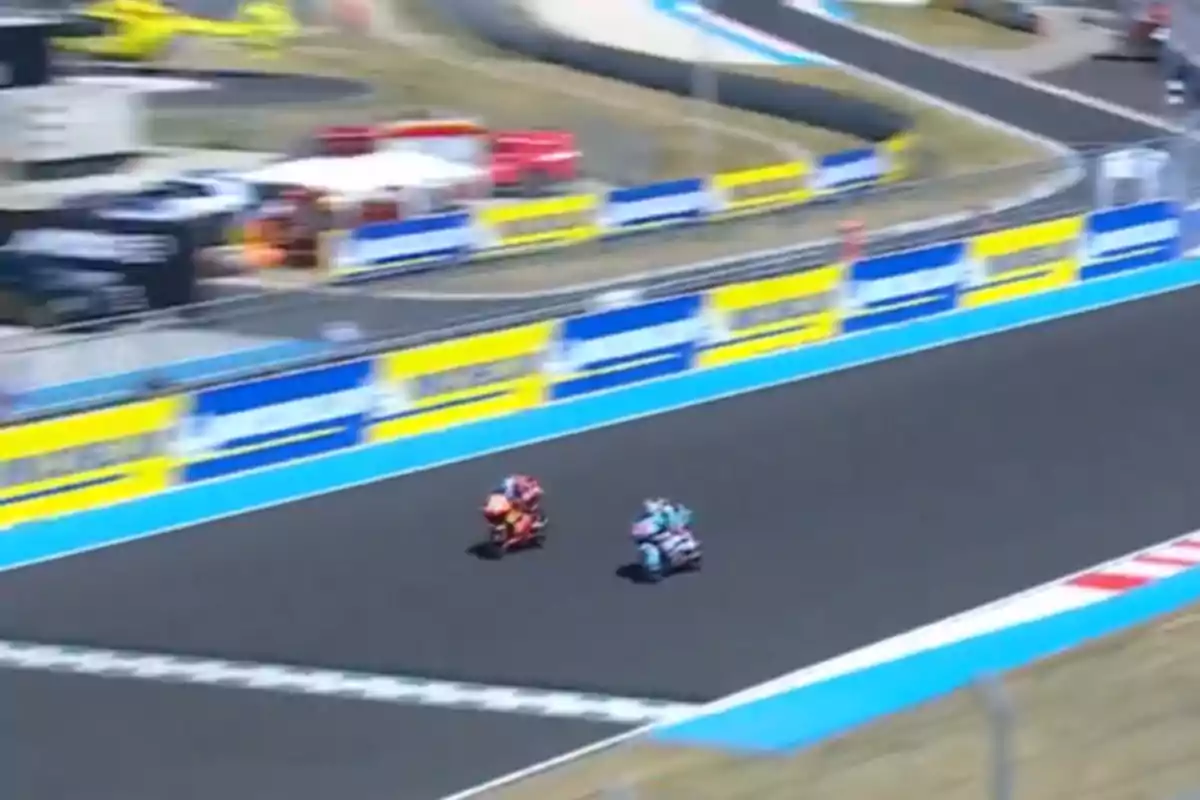 Dos motociclistas compiten en una pista de carreras asfaltada rodeada de vallas publicitarias y zonas de seguridad