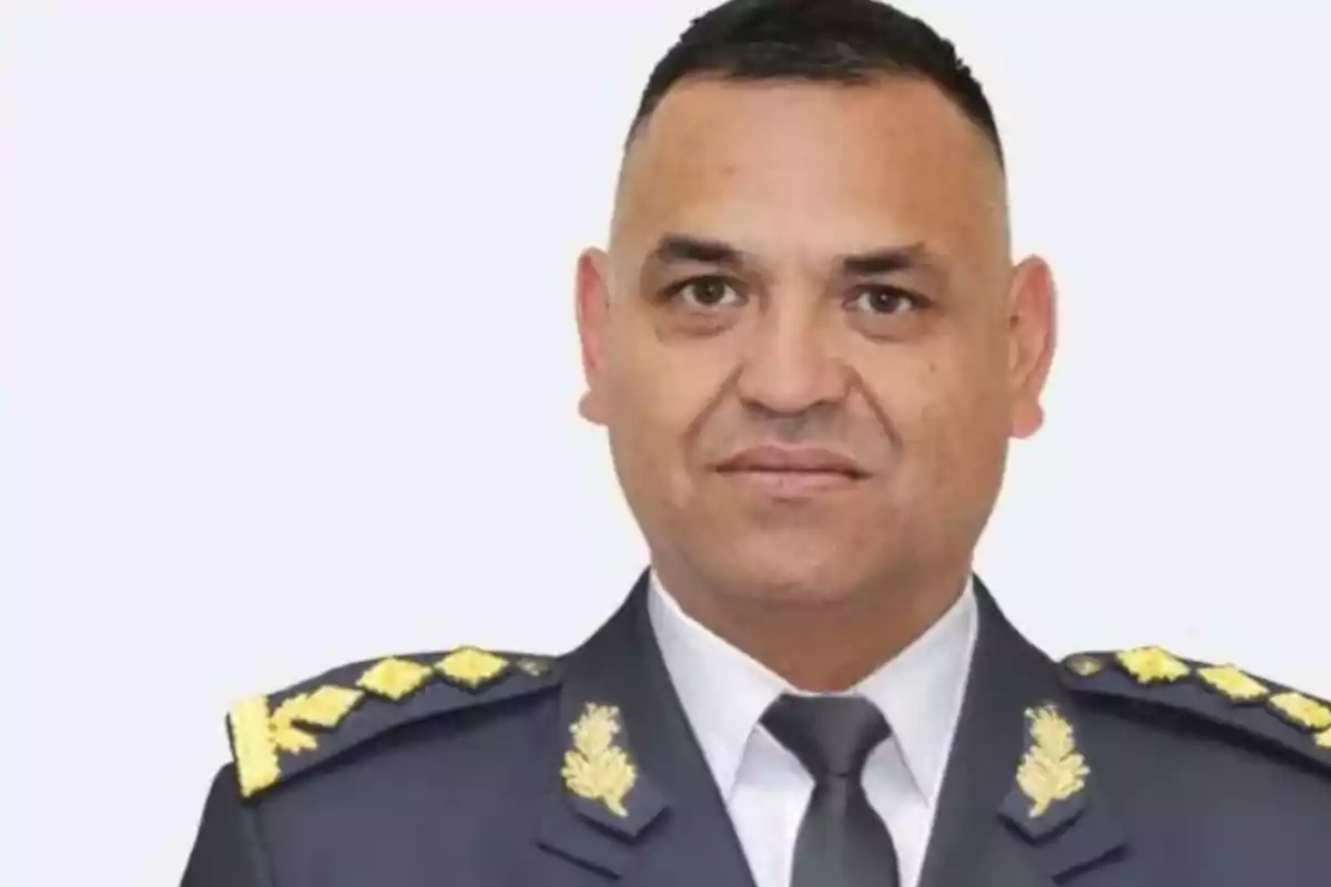 Man in a dark military uniform with gold epaulettes looking forward against a light background Man in a dark military uniform with gold epaulettes looking forward against a light background