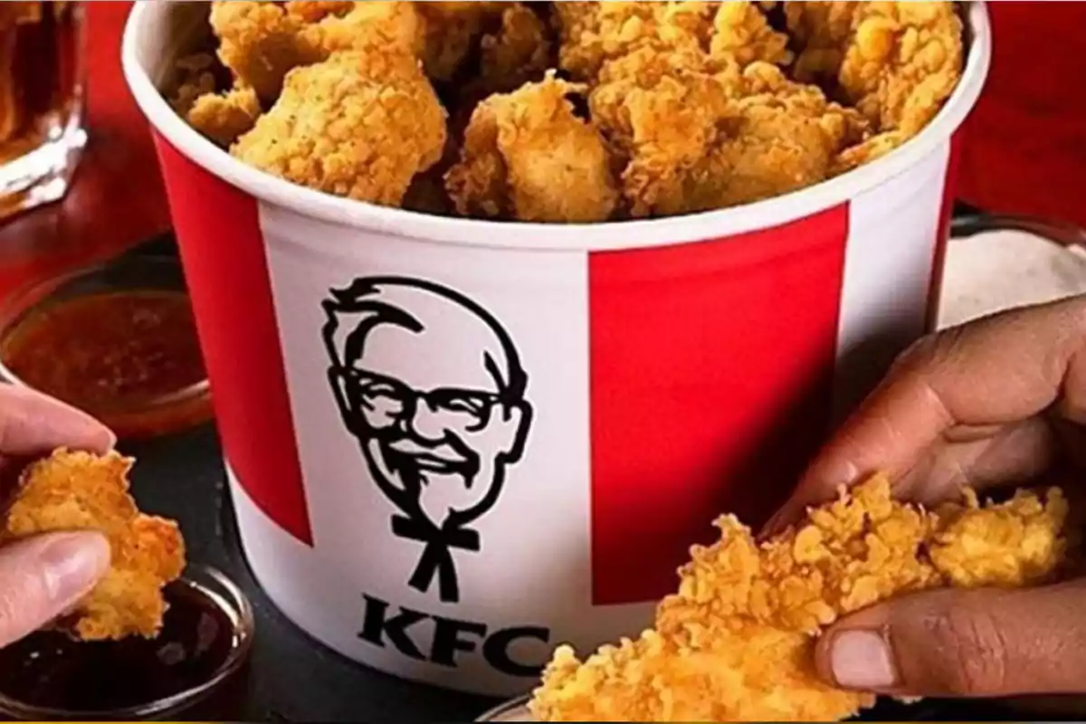People taking pieces of fried chicken from a KFC bucket with sauces in the background People taking pieces of fried chicken from a KFC bucket with sauces in the background