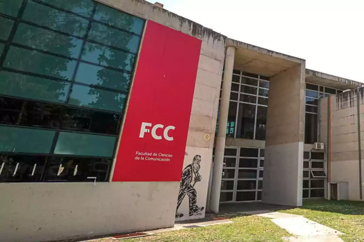 Fachada de un edificio moderno con un gran cartel rojo que dice FCC Facultad de Ciencias de la Comunicación y un mural de una persona caminando en la entrada Fachada de un edificio moderno con un gran cartel rojo que dice FCC Facultad de Ciencias de la Comunicación y un mural de una persona caminando en la entrada