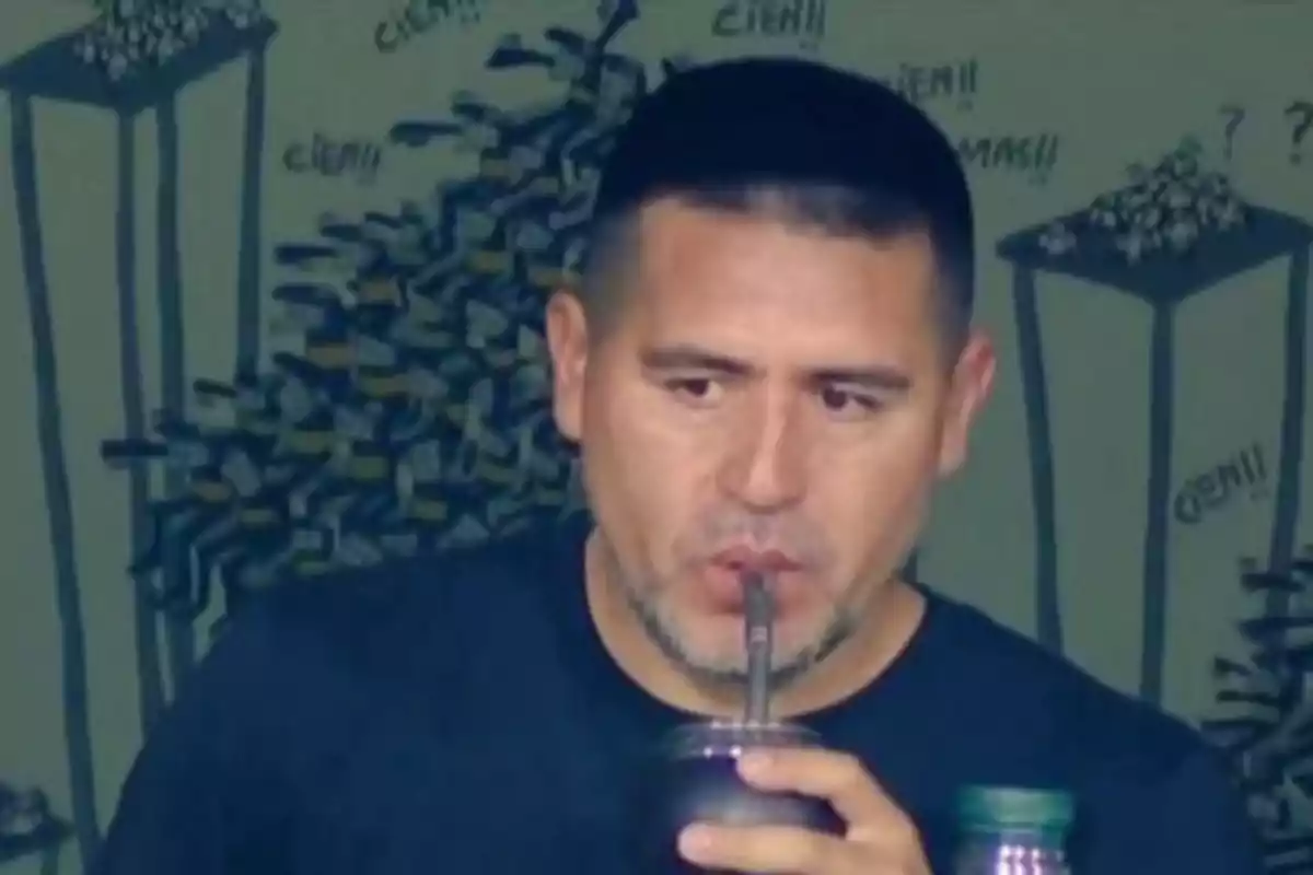 Short-haired man drinking mate with a straw in front of a wall decorated with drawings and words Short-haired man drinking mate with a straw in front of a wall decorated with drawings and words