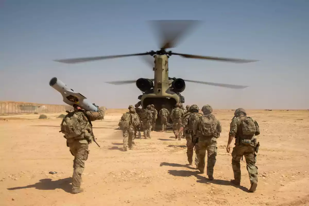 Soldiers with military gear walk toward a Chinook helicopter in the middle of the desert.