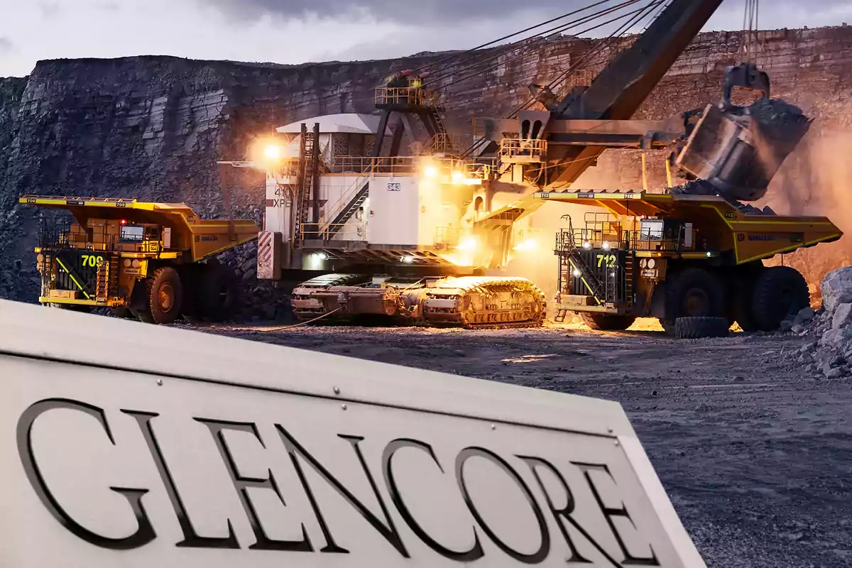 Heavy machinery working in an open-pit mine with trucks and an excavator; in the foreground, there is a sign with the name Glencore.