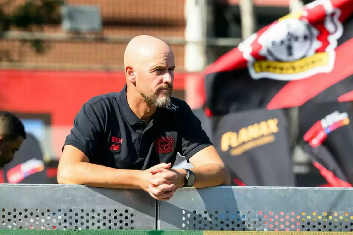 Bald man with a beard leaning on a metal fence during a sporting event with flags and a blurred background Bald man with a beard leaning on a metal fence during a sporting event with flags and a blurred background