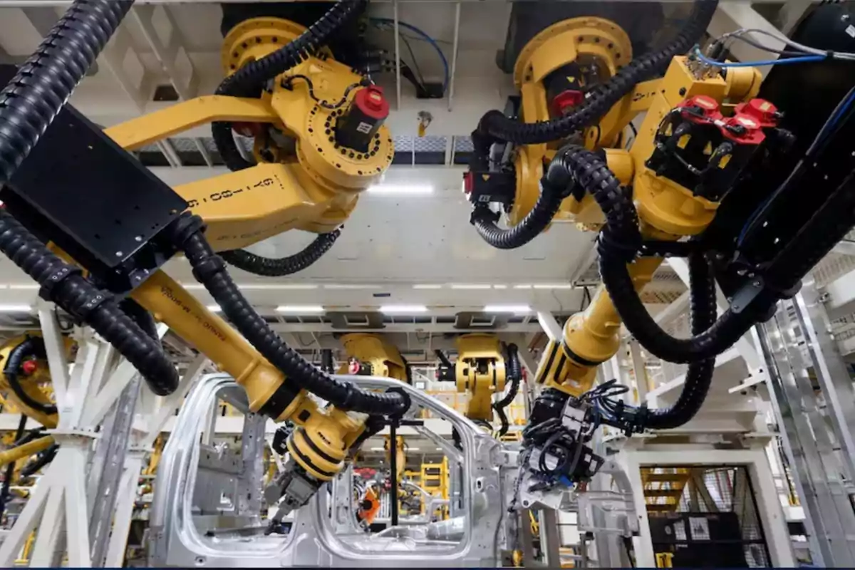 Brazos robóticos amarillos ensamblando la carrocería de un automóvil en una línea de producción industrial automatizada