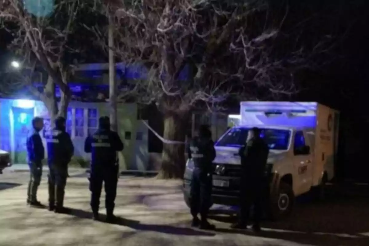 Varios policías y una camioneta de servicios forenses están frente a una casa acordonada durante la noche