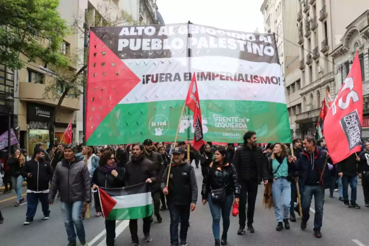 Manifestación en la calle con personas sosteniendo una gran pancarta y banderas en apoyo al pueblo palestino Manifestación en la calle con personas sosteniendo una gran pancarta y banderas en apoyo al pueblo palestino