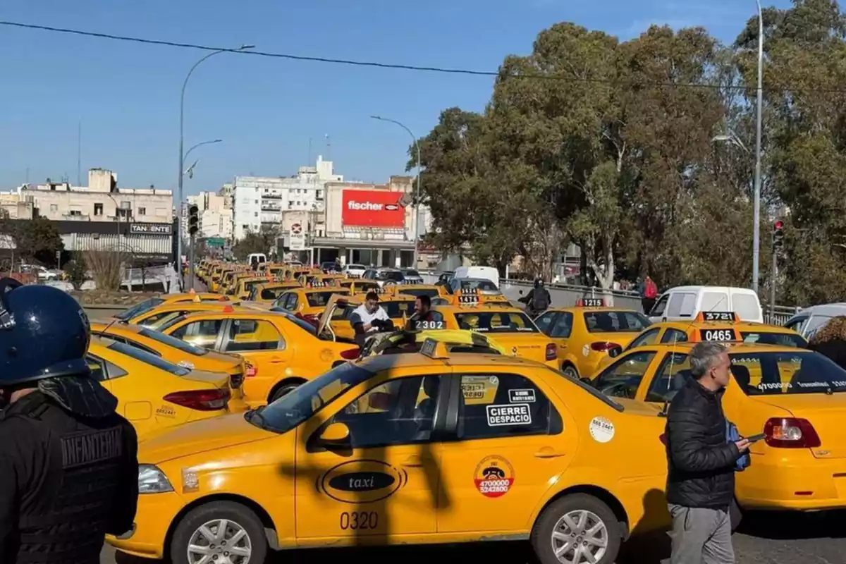 Varios taxis amarillos están detenidos en una calle mientras algunas personas caminan y conversan entre los autos en un día soleado Varios taxis amarillos están detenidos en una calle mientras algunas personas caminan y conversan entre los autos en un día soleado