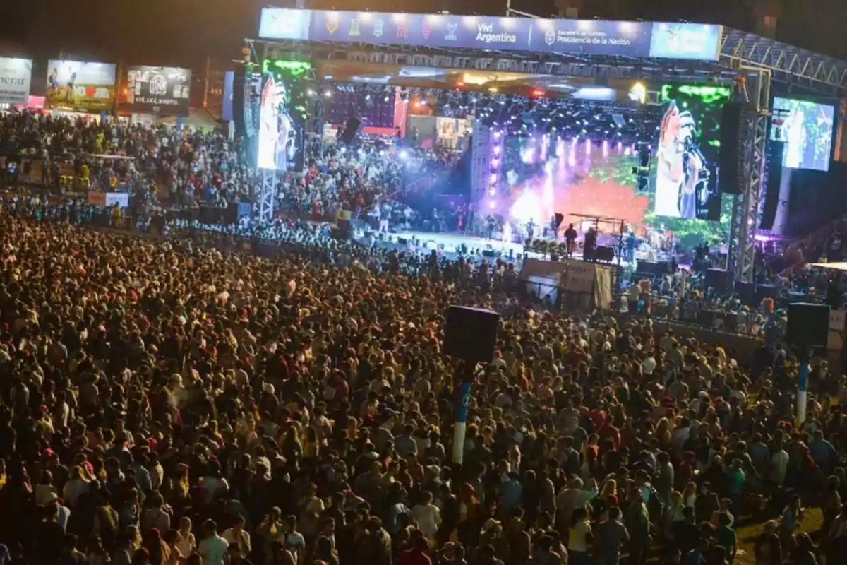 Miles de personas disfrutan de un concierto al aire libre frente a un gran escenario iluminado por luces de colores Miles de personas disfrutan de un concierto al aire libre frente a un gran escenario iluminado por luces de colores