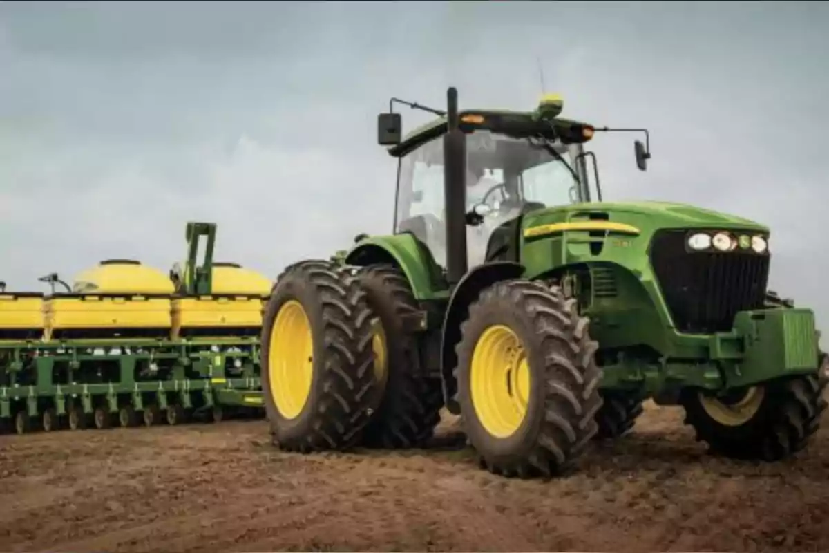 Green farm tractor with large tires and a yellow planter working in a dirt field under a cloudy sky