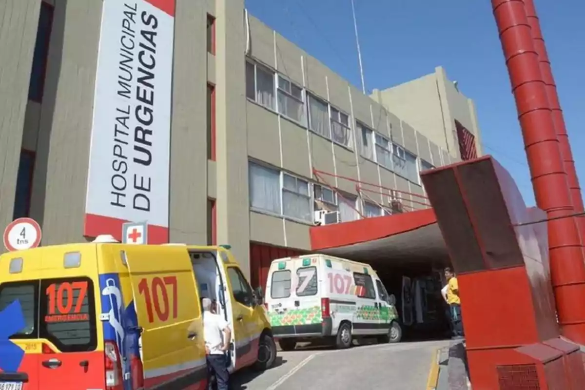 Fachada de un hospital de urgencias con ambulancias estacionadas en la entrada y personas cerca de los vehículos Fachada de un hospital de urgencias con ambulancias estacionadas en la entrada y personas cerca de los vehículos