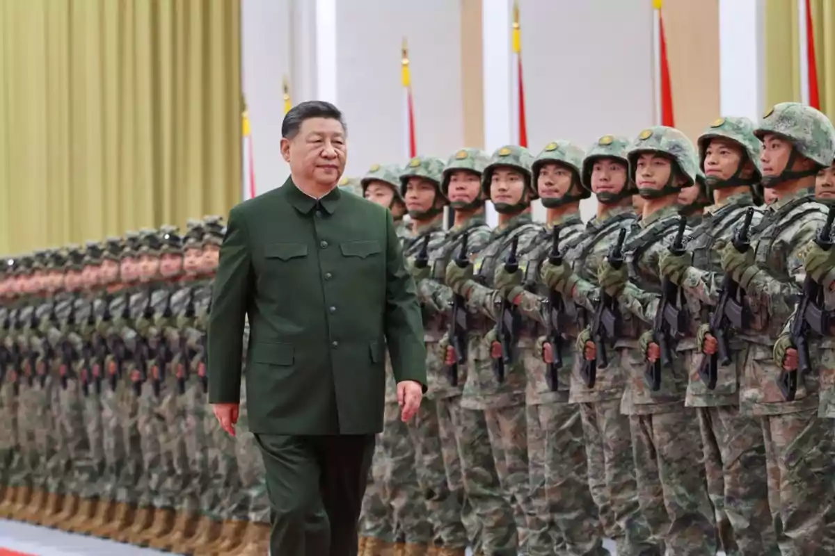 A man in a green military uniform walks in front of a row of soldiers lined up wearing helmets and carrying weapons in a hall with flags and yellow curtains in the background. A man in a green military uniform walks in front of a row of soldiers lined up wearing helmets and carrying weapons in a hall with flags and yellow curtains in the background.