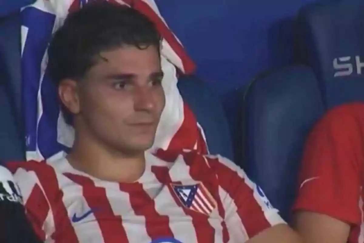 Jugador del Atlético de Madrid sentado en la banca con expresión seria y una toalla sobre los hombros Jugador del Atlético de Madrid sentado en la banca con expresión seria y una toalla sobre los hombros