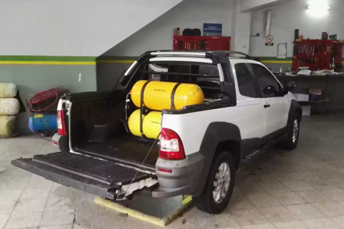 Camioneta blanca con dos tanques de gas amarillos instalados en la caja trasera dentro de un taller mecánico