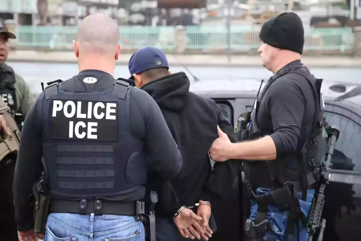 Police officers detain a handcuffed person next to a vehicle