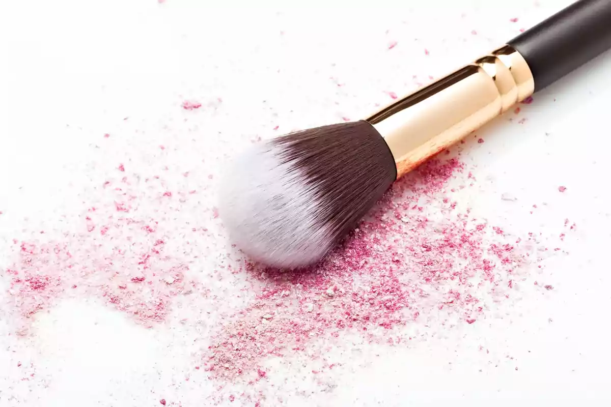Brocha de maquillaje sobre polvo rosa esparcido en una superficie blanca Brocha de maquillaje sobre polvo rosa esparcido en una superficie blanca