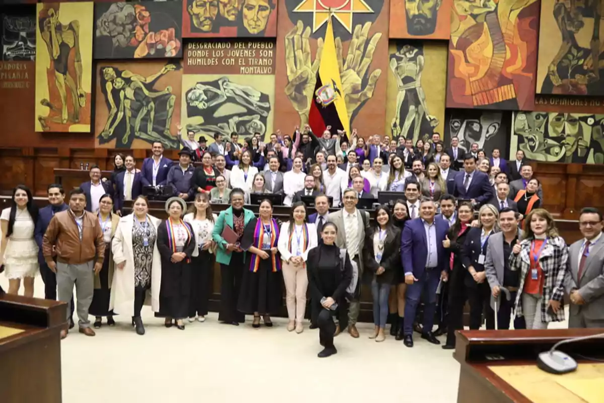 Un grupo numeroso de personas posando para una foto en el interior de un recinto con murales coloridos y una bandera de Ecuador al fondo Un grupo numeroso de personas posando para una foto en el interior de un recinto con murales coloridos y una bandera de Ecuador al fondo
