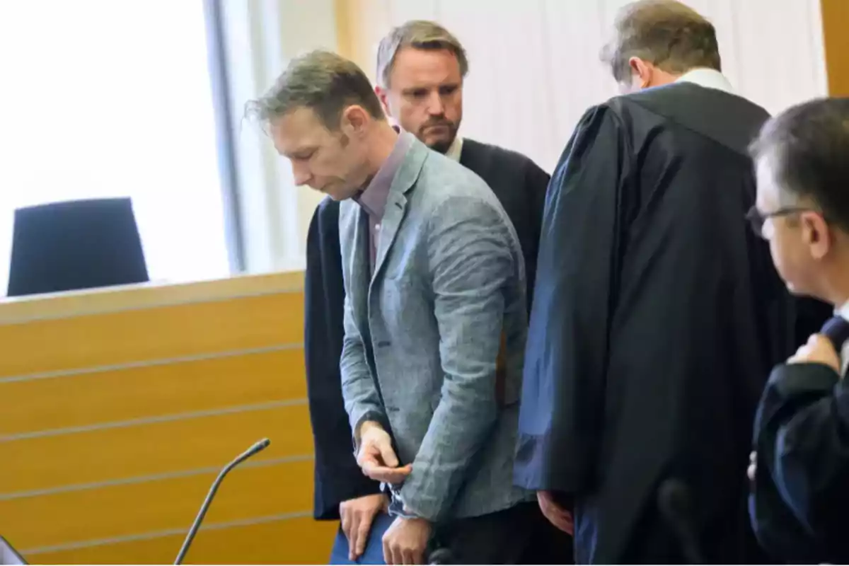 Un hombre esposado con la cabeza baja está rodeado de personas con toga en una sala de tribunal Un hombre esposado con la cabeza baja está rodeado de personas con toga en una sala de tribunal